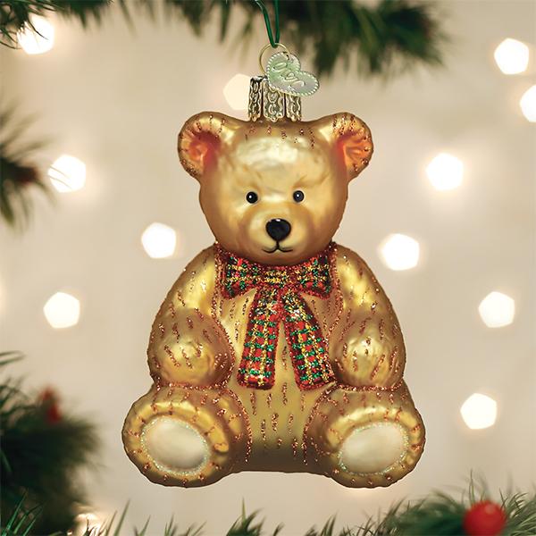 Golden teddy bear ornament hanging on a lit Christmas tree with warm bokeh lights