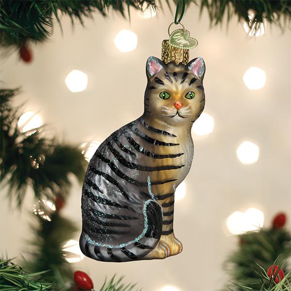 Tabby cat ornament hanging on a Christmas tree with warm twinkle lights glowing behind it