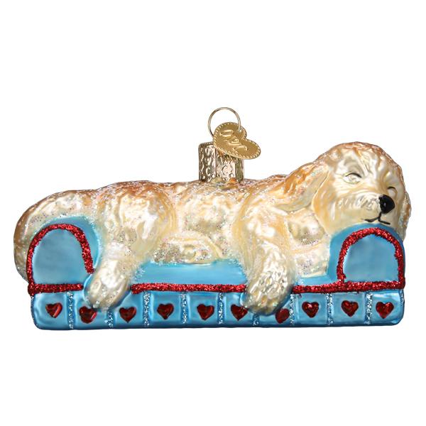 Cream doodle dog ornament asleep on a blue glass couch with red glitter trim and heart details, front view