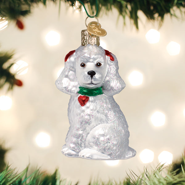 White poodle Christmas ornament hanging on a tree branch with warm bokeh lights