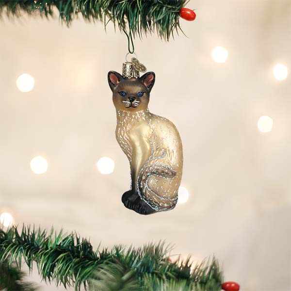 Siamese cat ornament hanging on a Christmas tree with warm holiday lights behind it