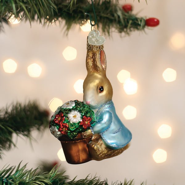 Peter Rabbit with flower pot ornament hanging on a lit Christmas tree with warm bokeh lights