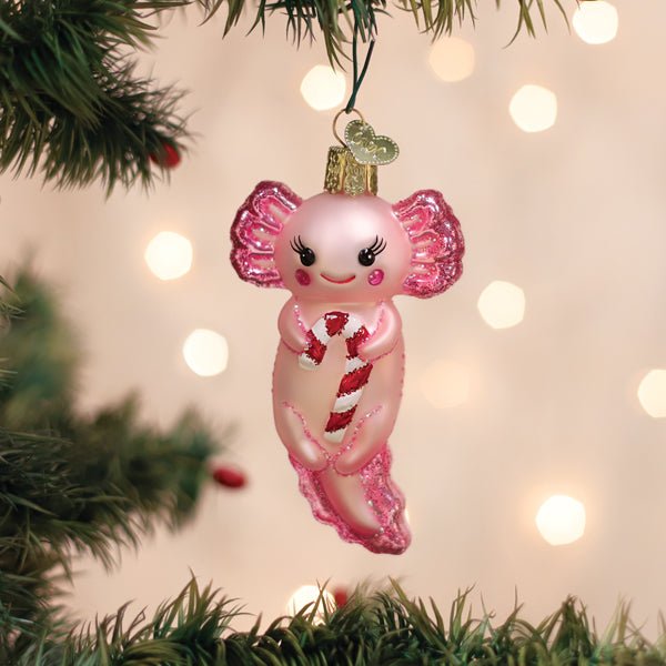 Pink axolotl ornament with a candy cane hanging on a lit Christmas tree with warm bokeh lights