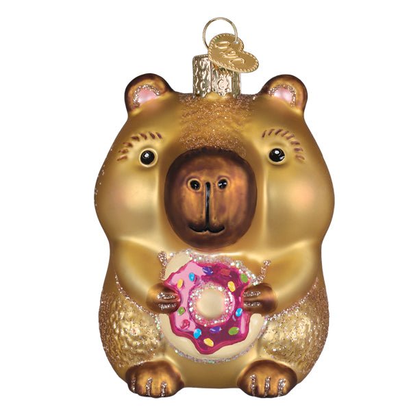 Capybara ornament holding a pink frosted donut with rainbow sprinkles, golden tan with glittered fur, front view on white