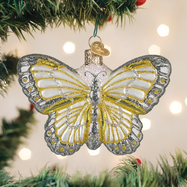 Silver and gold butterfly ornament hanging on a Christmas tree with warm lights behind