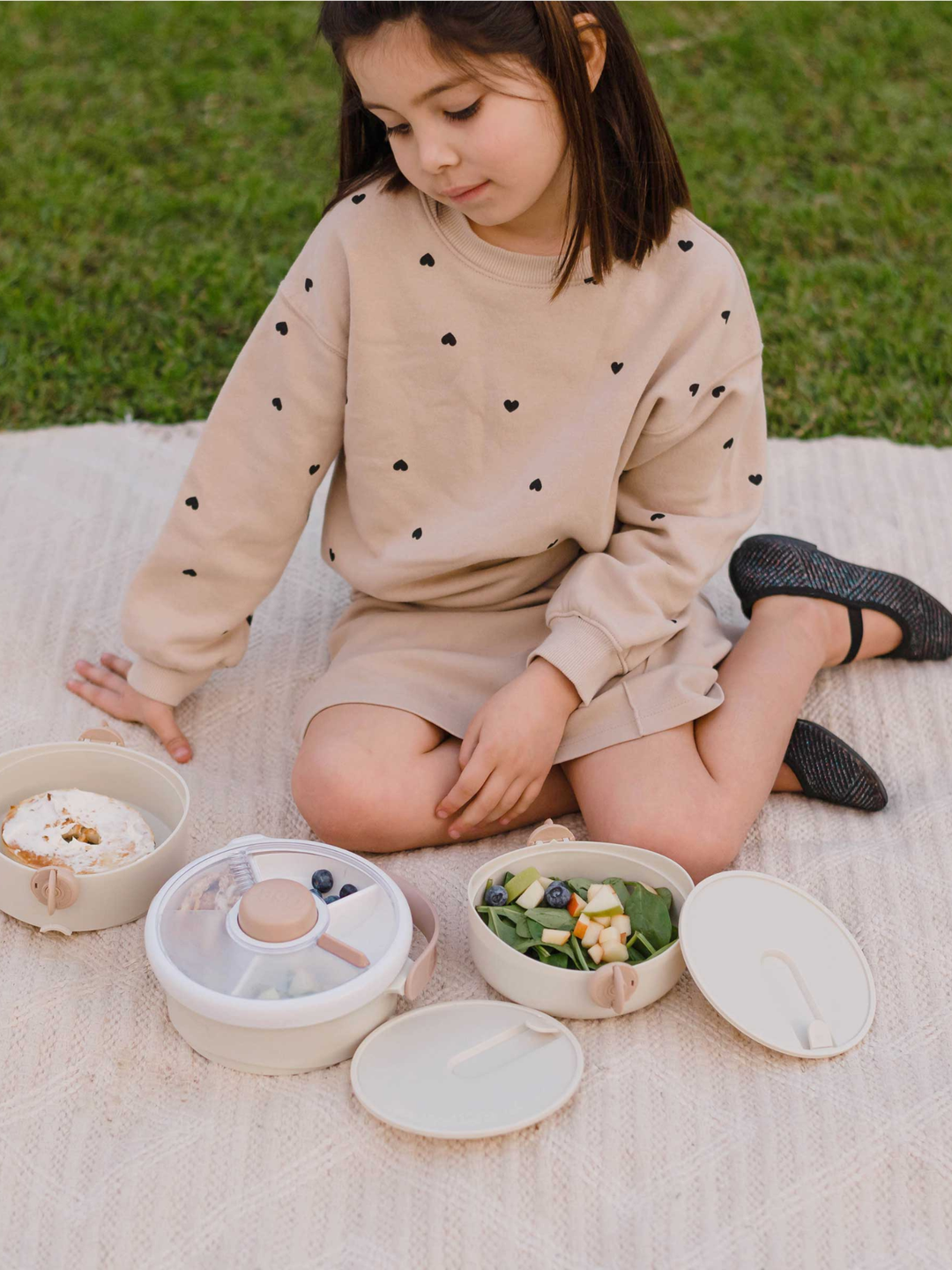 Girl on a picnic blanket reaching into the open cream Lunch Stack compartments