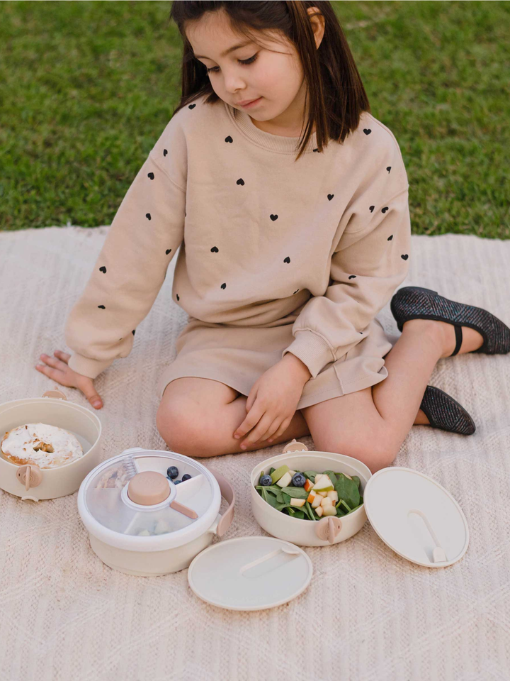Girl on a picnic blanket reaching into the open cream Lunch Stack compartments