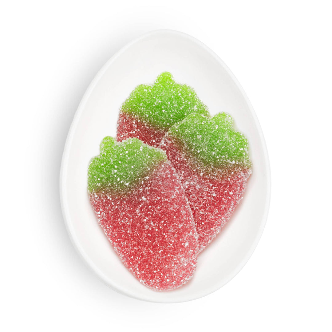 Red and green gummy strawberry candy leaves on a white plate