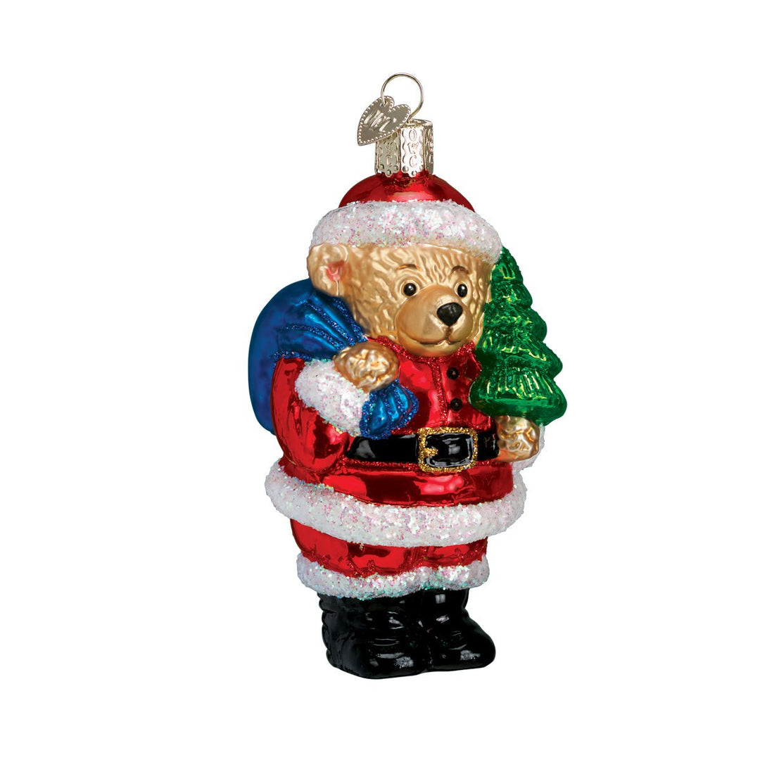 Teddy bear in a red Santa suit and black boots holding a blue toy sack and a green tree, on white