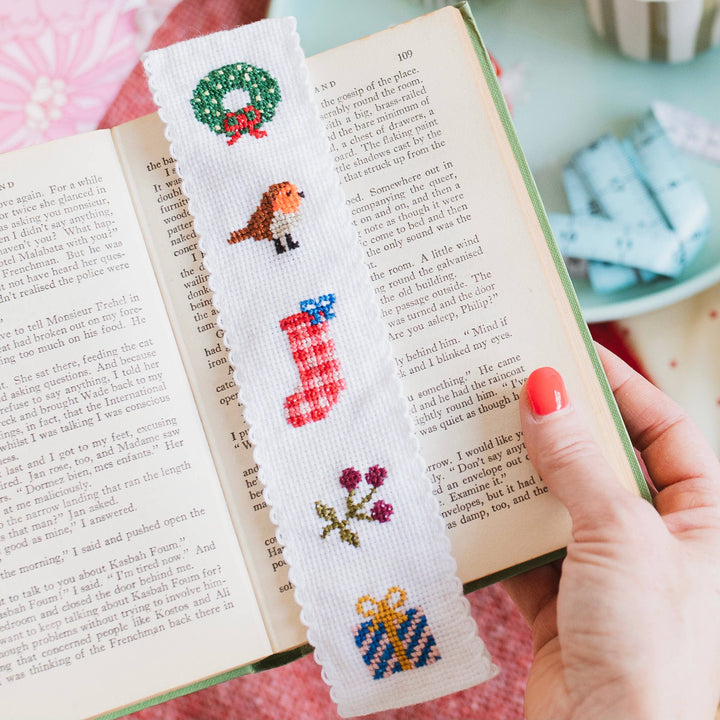 Hand holding an open book with the Christmas cross stitch bookmark inside