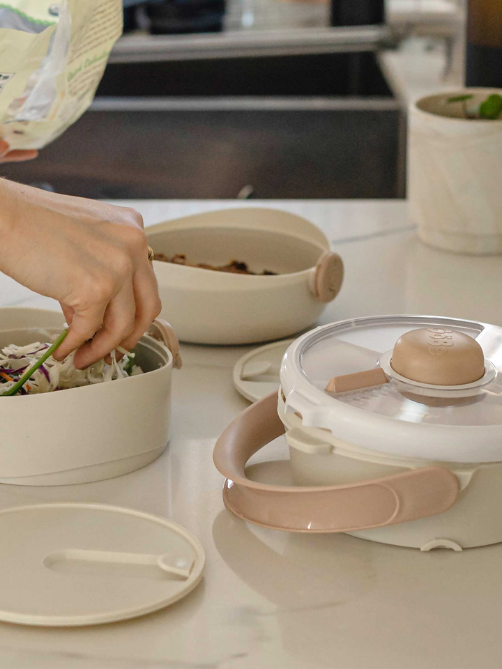 Hands packing salad into the cream Lunch Stack meal compartments