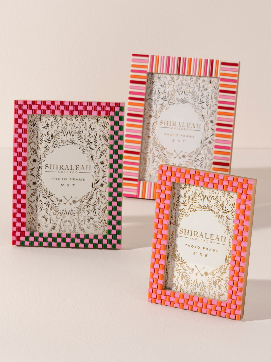 Three picture frames leaning on a cream surface, a red and white check, a multicolor stripe, and a pink and red check