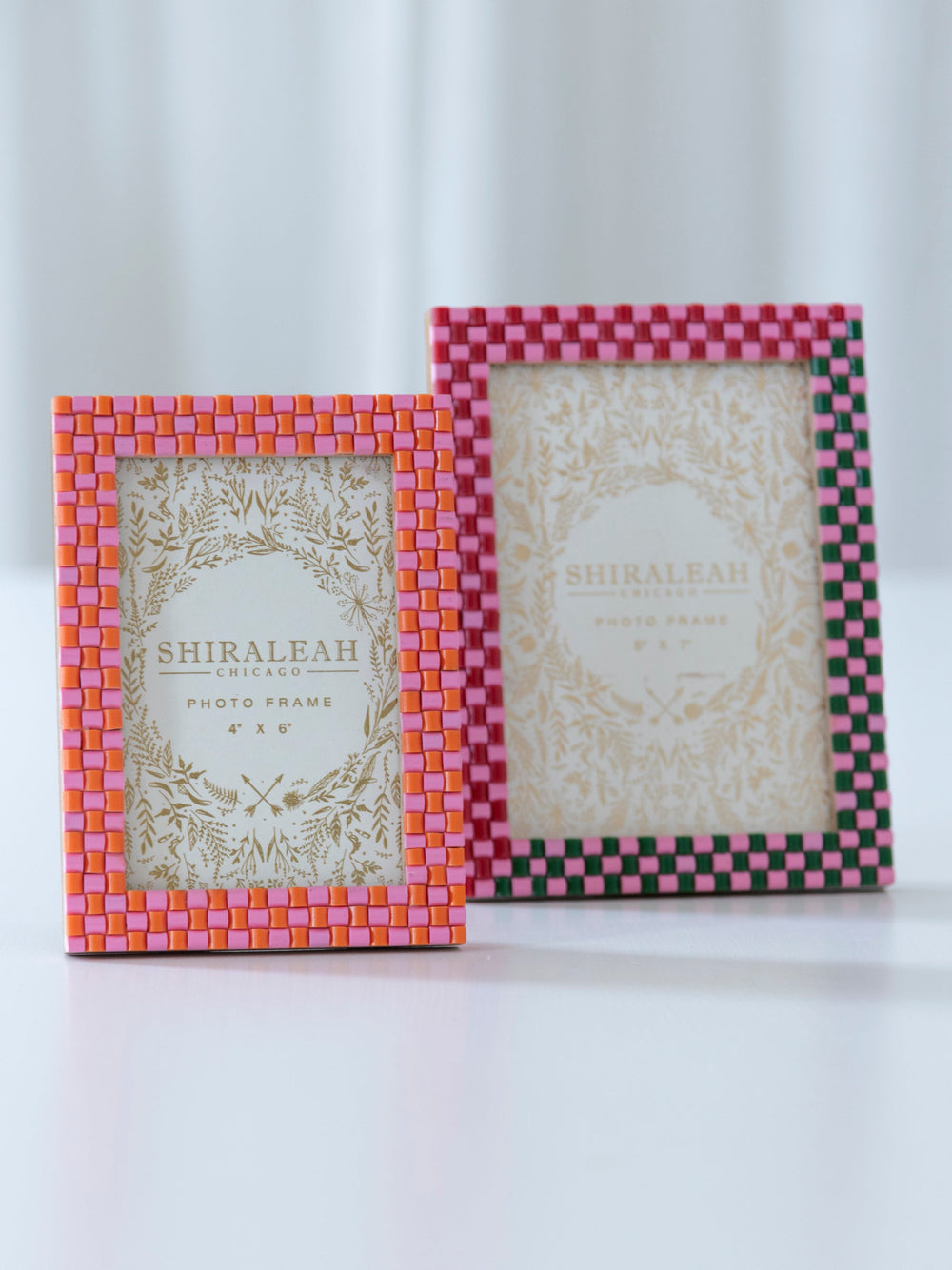 Two checkerboard picture frames on a soft white surface, one in pink and red and one in pink and dark plum