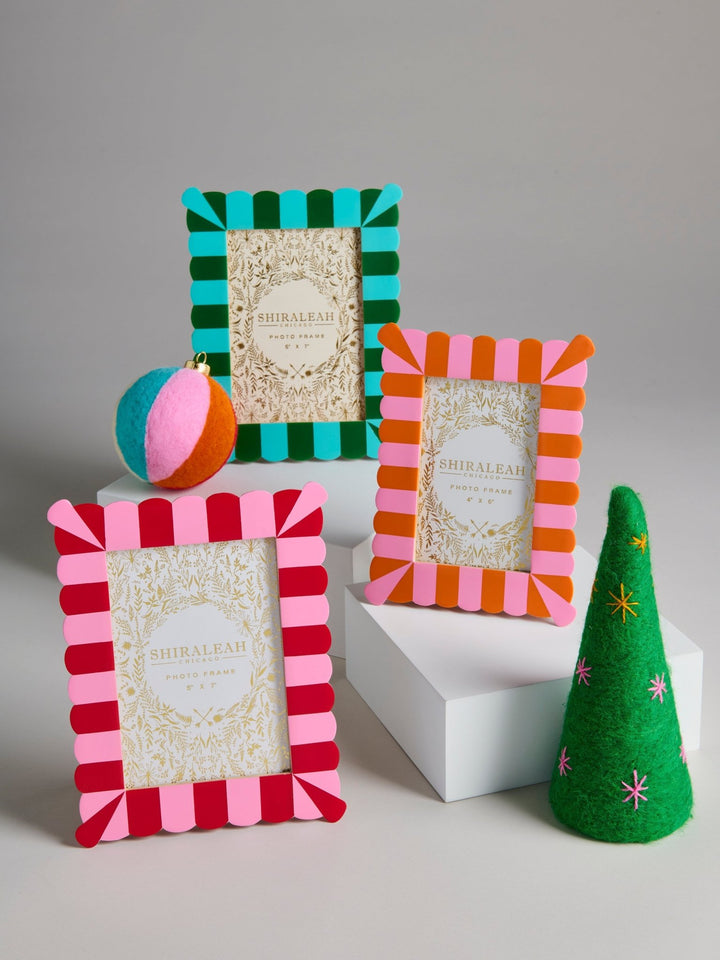 Three decorative photo frames with striped felt edges in teal and green, pink and orange, and red and pink, displayed on white blocks with a small green felt tree and a striped ball prop against a light gray background.