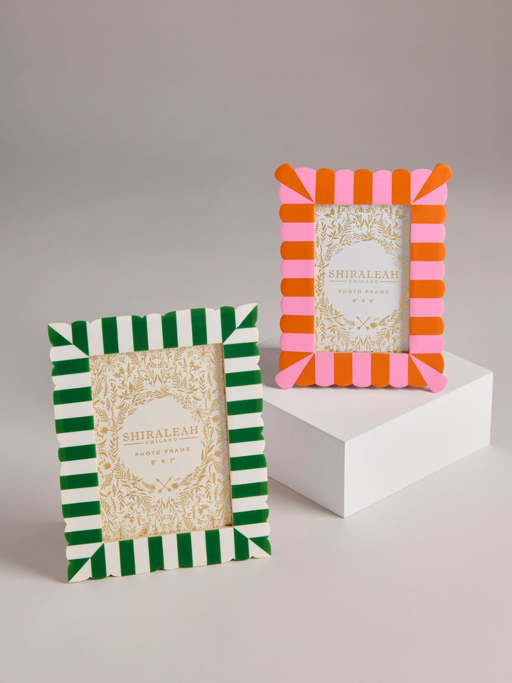Two decorative picture frames with striped borders are displayed on a light gray background, with one frame standing on a white pedestal. The left frame has green and white stripes, and the right frame has pink and orange stripes.