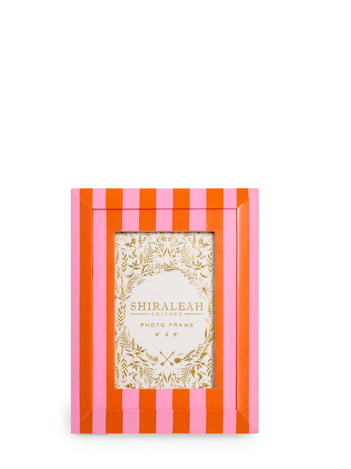 A rectangular Shiraleah photo frame with alternating pink and orange vertical stripes, featuring a central clear window with a gold botanical wreath design and the brand name printed inside.