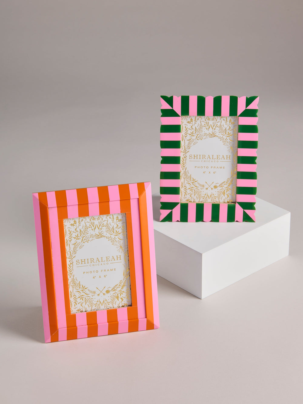 Two decorative picture frames with striped borders are displayed on a light gray studio background. One frame has vertical pink and orange stripes, and the other has diagonal green and pink stripes.