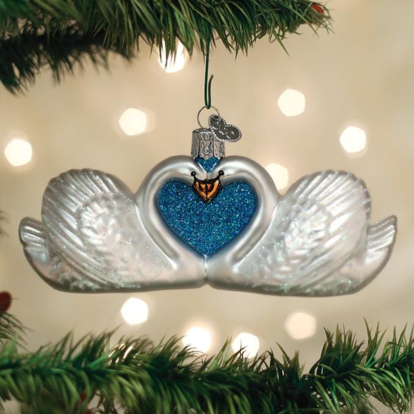 Swans in love Christmas ornament hanging on a tree branch with warm bokeh lights