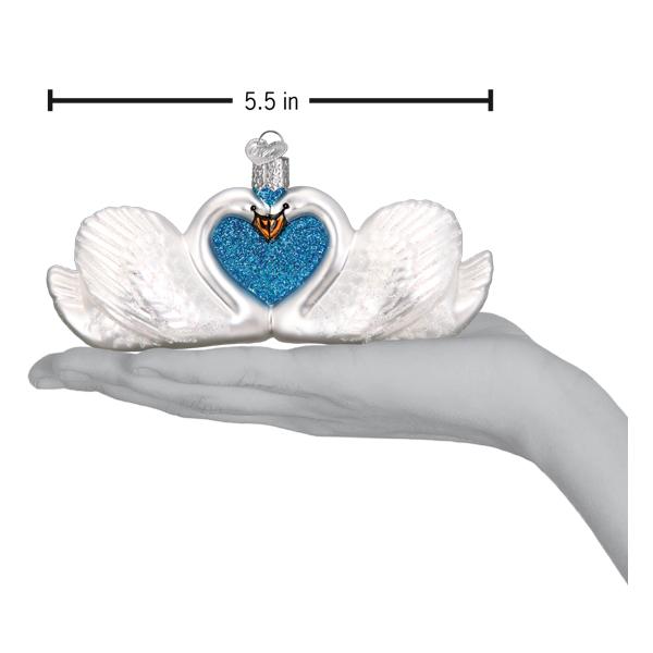 Swans in love ornament held above an open palm with a 5.5 inch width marker for scale