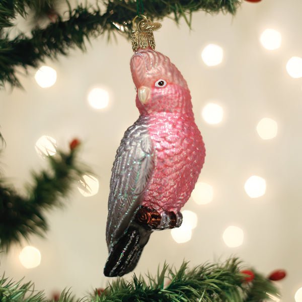 Pink cockatoo ornament hanging on a lit Christmas tree with glowing bokeh lights behind