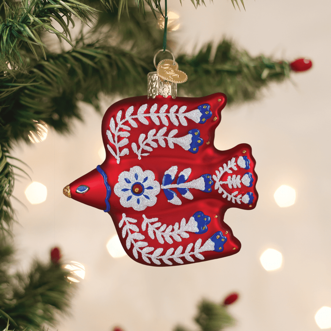 Red folk art bird ornament hanging on a lit Christmas tree with warm bokeh lights