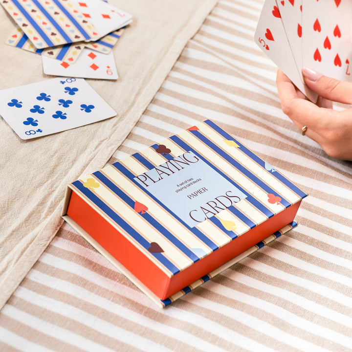 Striped playing card box on a table as players hold hands of cards, ready for a holiday game night