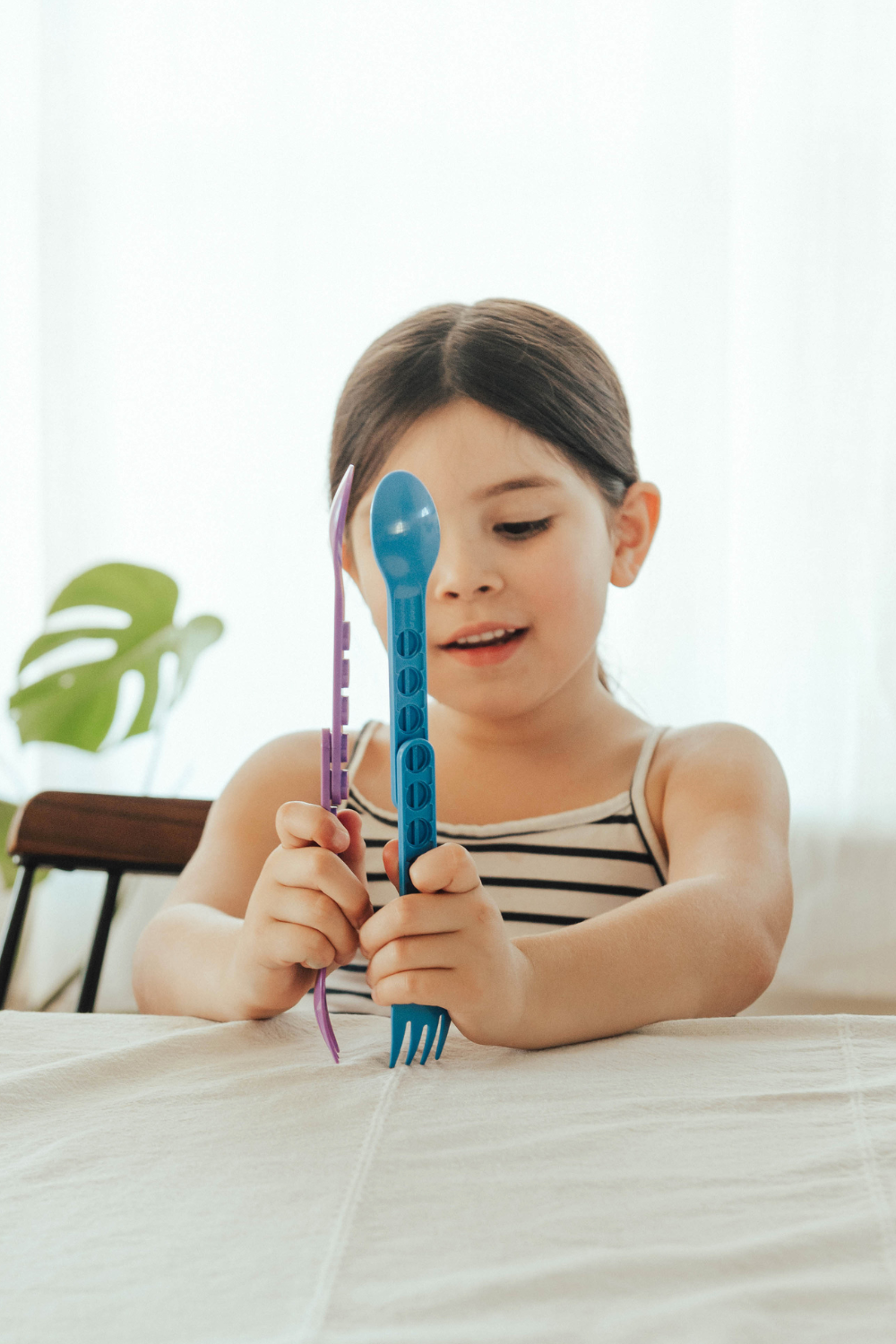 Girl at a table holding up a blue GoBe fork and spoon