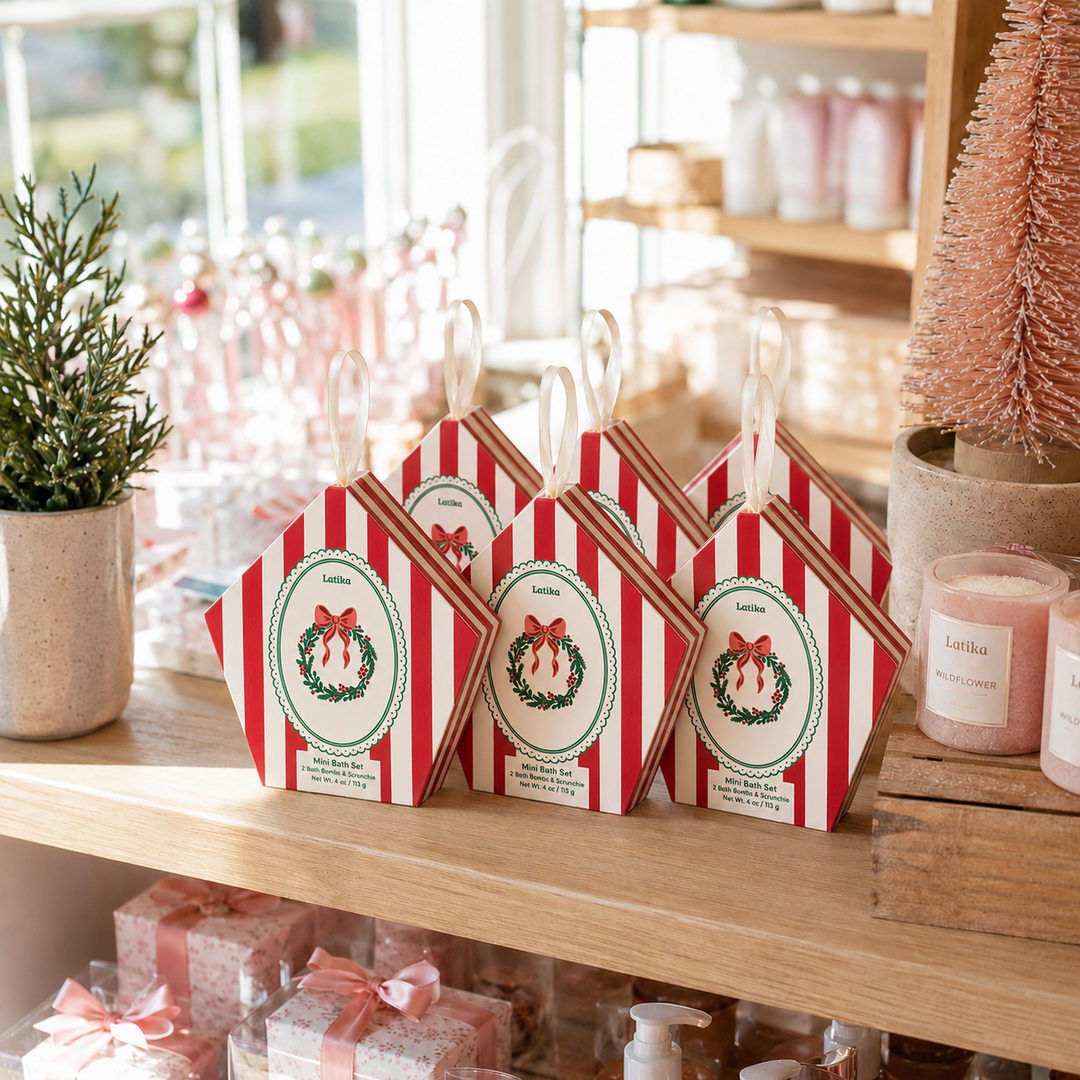 Three red striped wreath ornament boxes on a boutique shelf with candles and a mini tree for holiday shopping