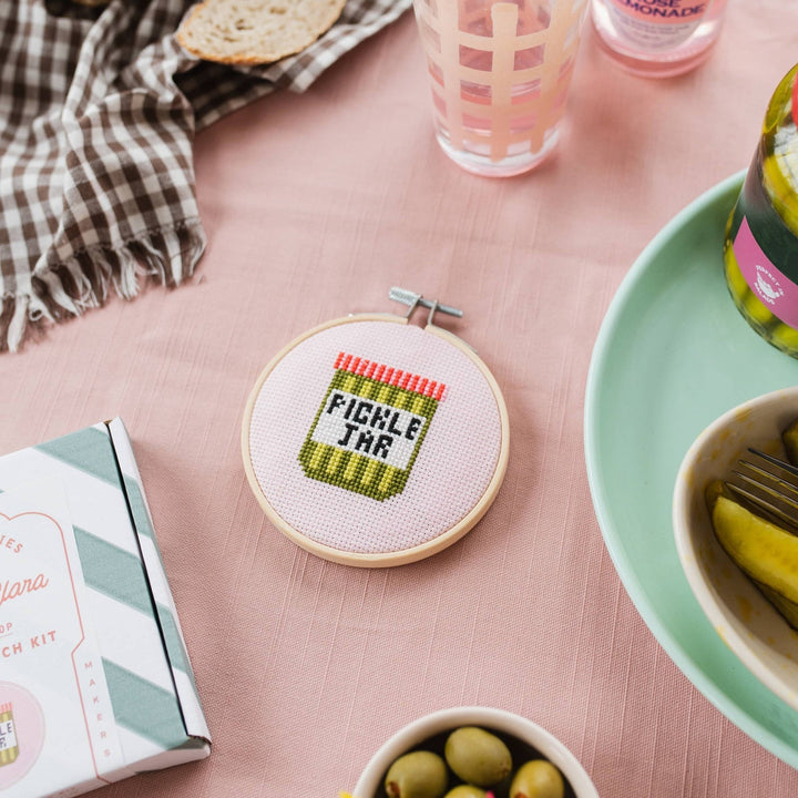 Pickle jar cross stitch hoop beside the kit box at a snack table