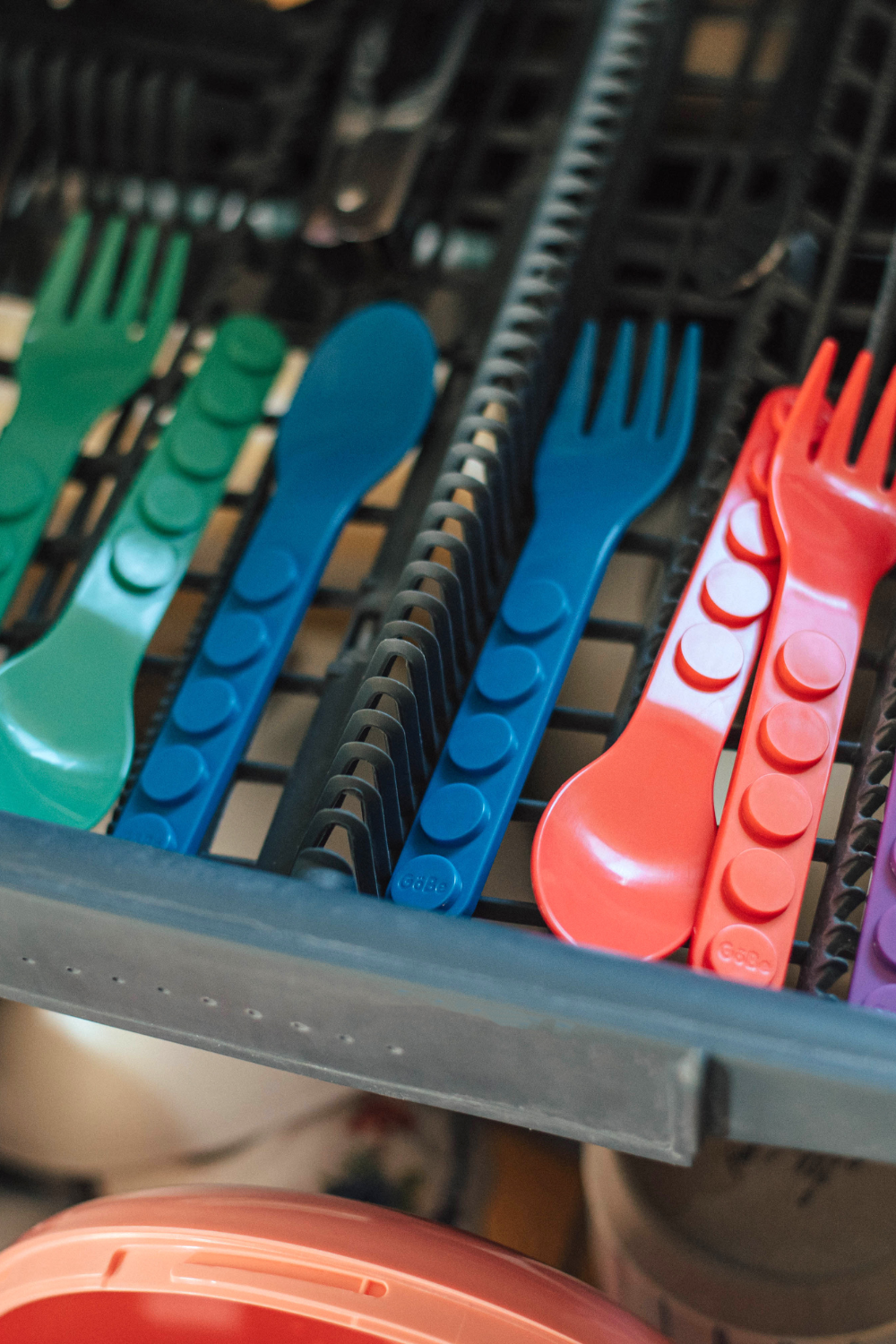 Blue, green, and red GoBe utensils standing in a dishwasher basket