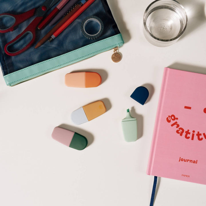 Highlighters scattered by a pencil pouch and pink gratitude journal, an easy stocking stuffer for students