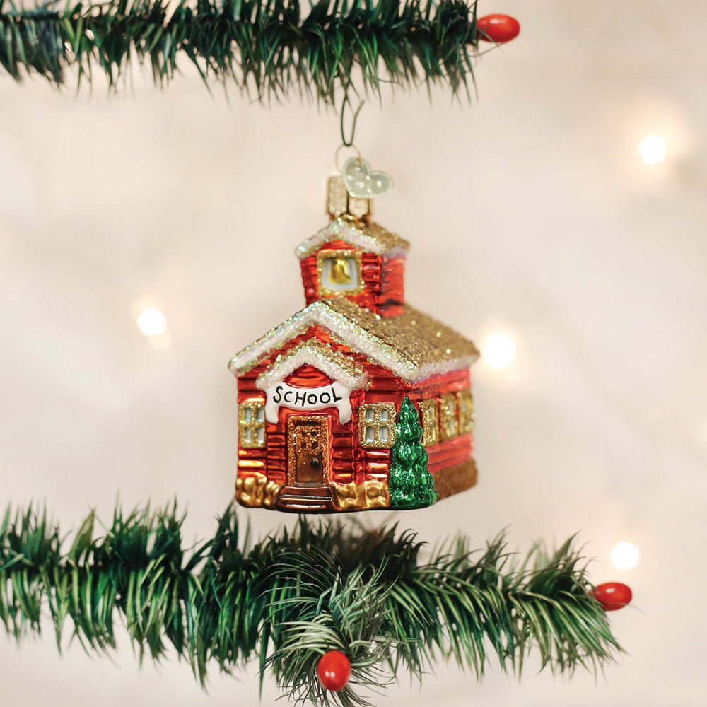 Schoolhouse ornament hanging on a pine branch with red berries and soft lights, a teacher's Christmas gift