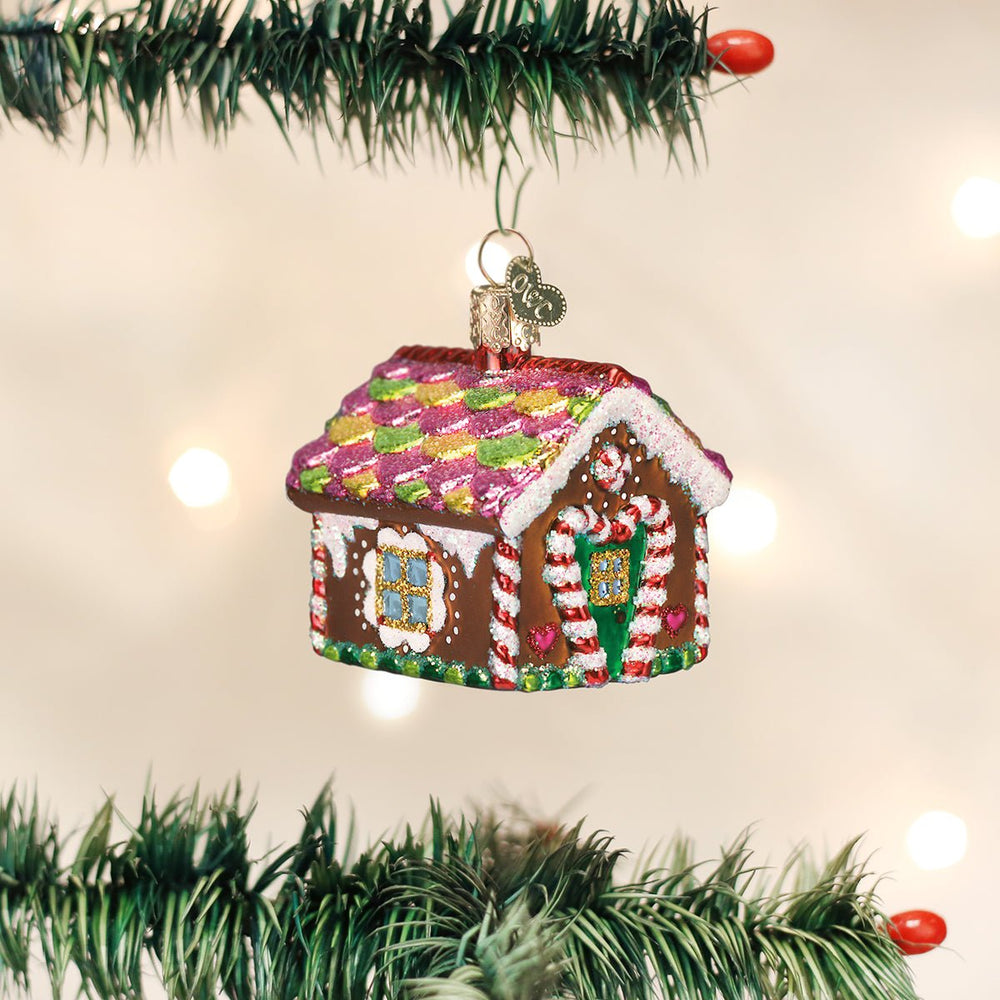 Small gingerbread house glass ornament hanging from a lit Christmas tree