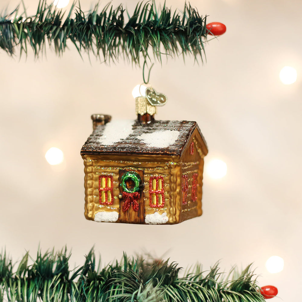 Log cabin ornament hanging between garland branches with warm twinkle lights