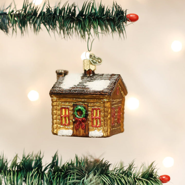 Log cabin ornament hanging between garland branches with warm twinkle lights