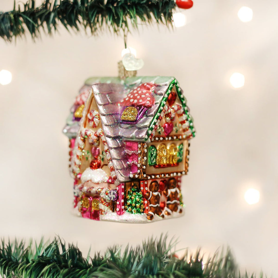 Cupcake cottage glass ornament hanging on a lit Christmas tree with gold bokeh