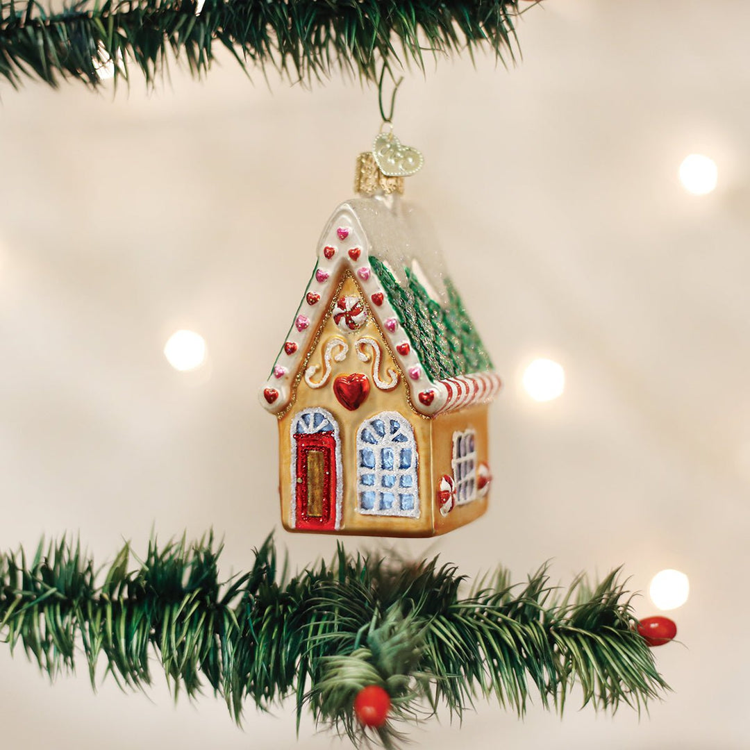 Gingerbread cookie cottage ornament hanging between garland branches with warm bokeh lights