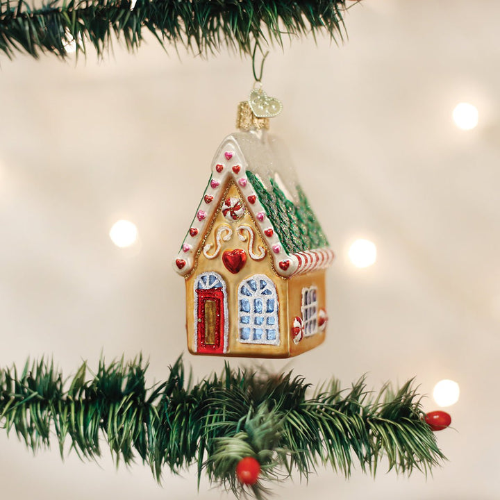 Gingerbread cookie cottage ornament hanging between garland branches with warm bokeh lights