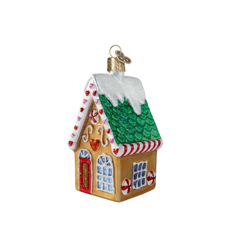 Gingerbread cookie cottage glass ornament with green shingle roof and snowy icing, angled front on white
