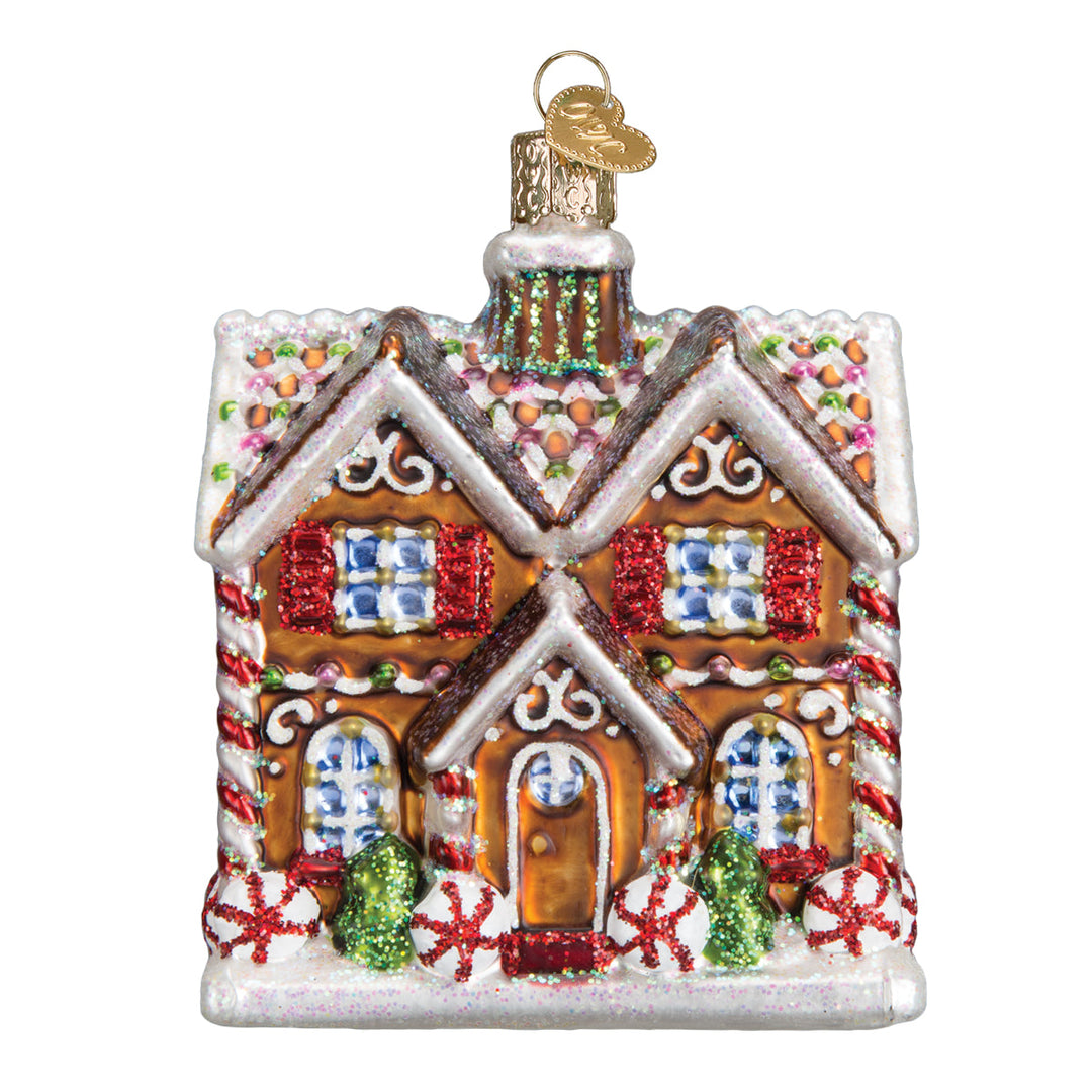 Christmastime cottage glass ornament with snowy twin gables, red shutters, and peppermint trim, front on white