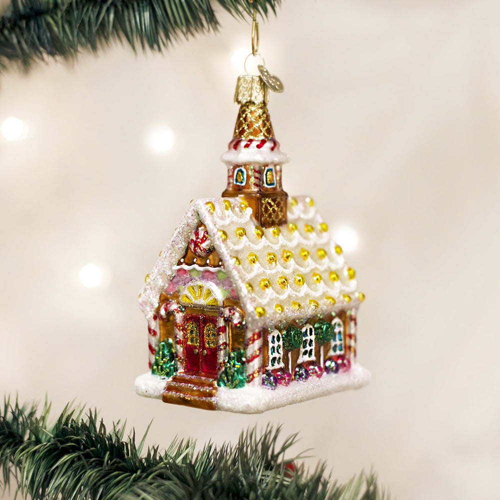 Gingerbread church glass ornament with a tall steeple hanging on a lit Christmas tree