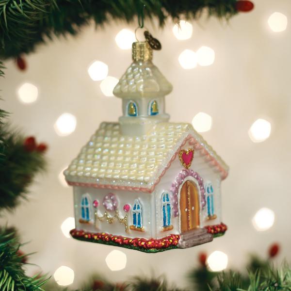 White wedding chapel glass ornament with a steeple and pink heart, hanging on a lit Christmas tree