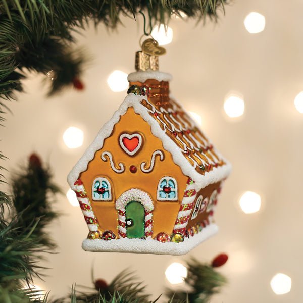 Gingerbread cottage glass ornament with peppermint trim hanging on a lit Christmas tree