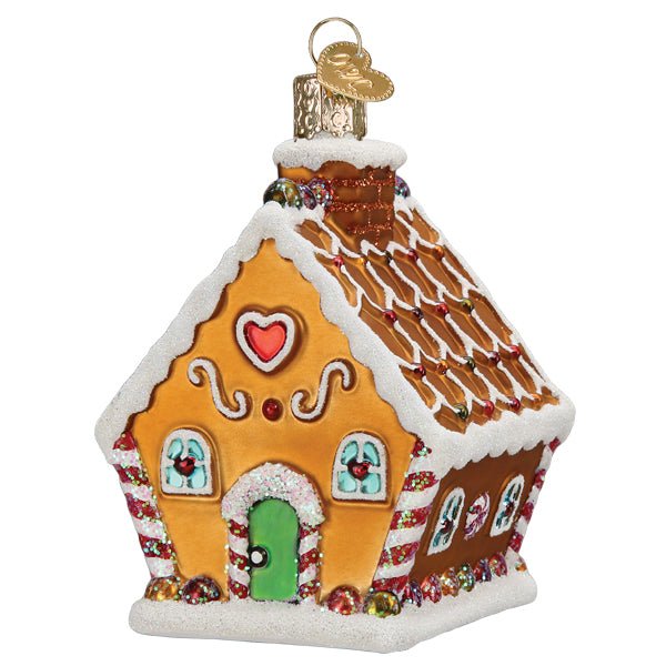 Front of the gingerbread cottage ornament with white icing, a red heart, and a green door, on white