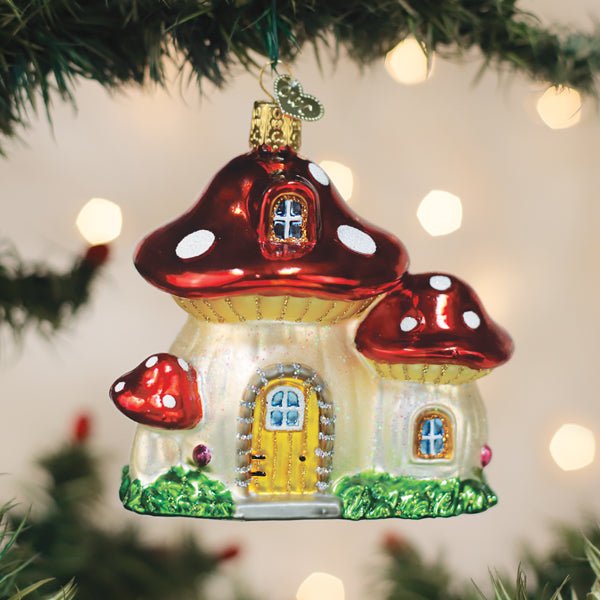 Mushroom house ornament hanging on a lit Christmas tree with warm bokeh lights