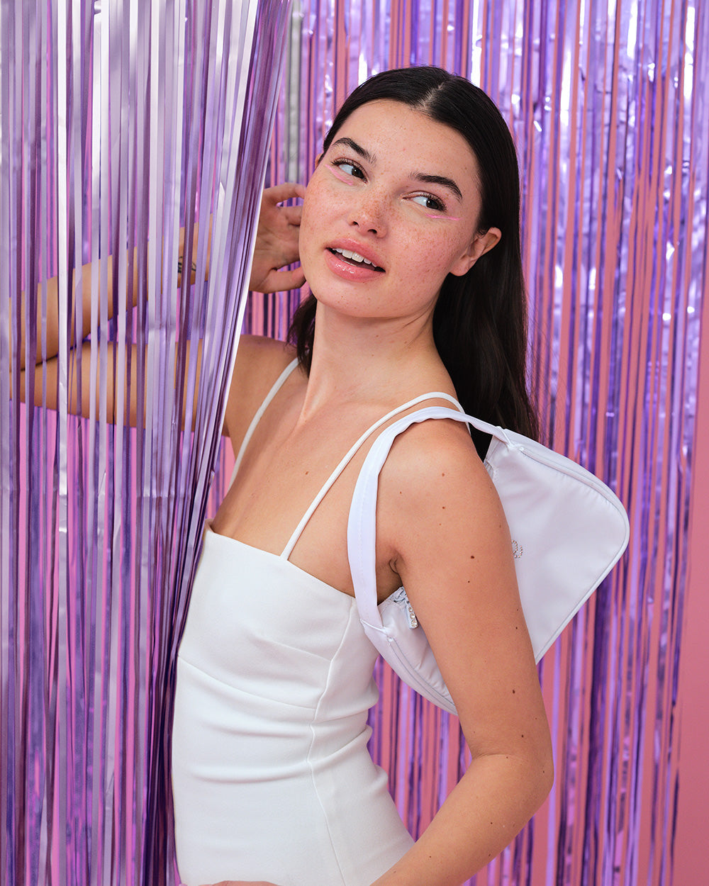 Model in a white dress standing beside a purple foil fringe curtain photo backdrop