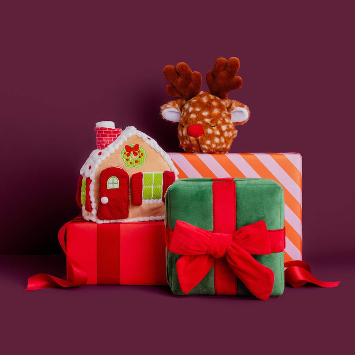 Present toy with a gingerbread house toy and reindeer toy stacked on wrapped gifts against plum