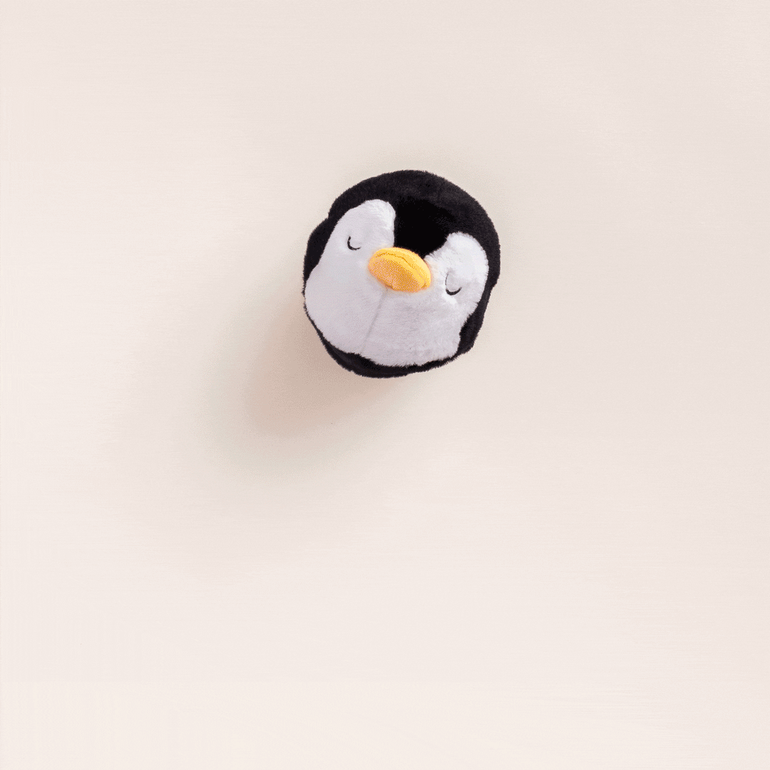 Penguin plush dog toy seen from above on a pale pink background.