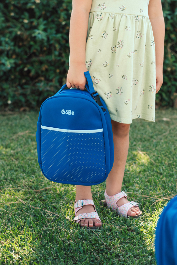 Girl in a floral dress carrying the blue GoBe lunch bag by its handle