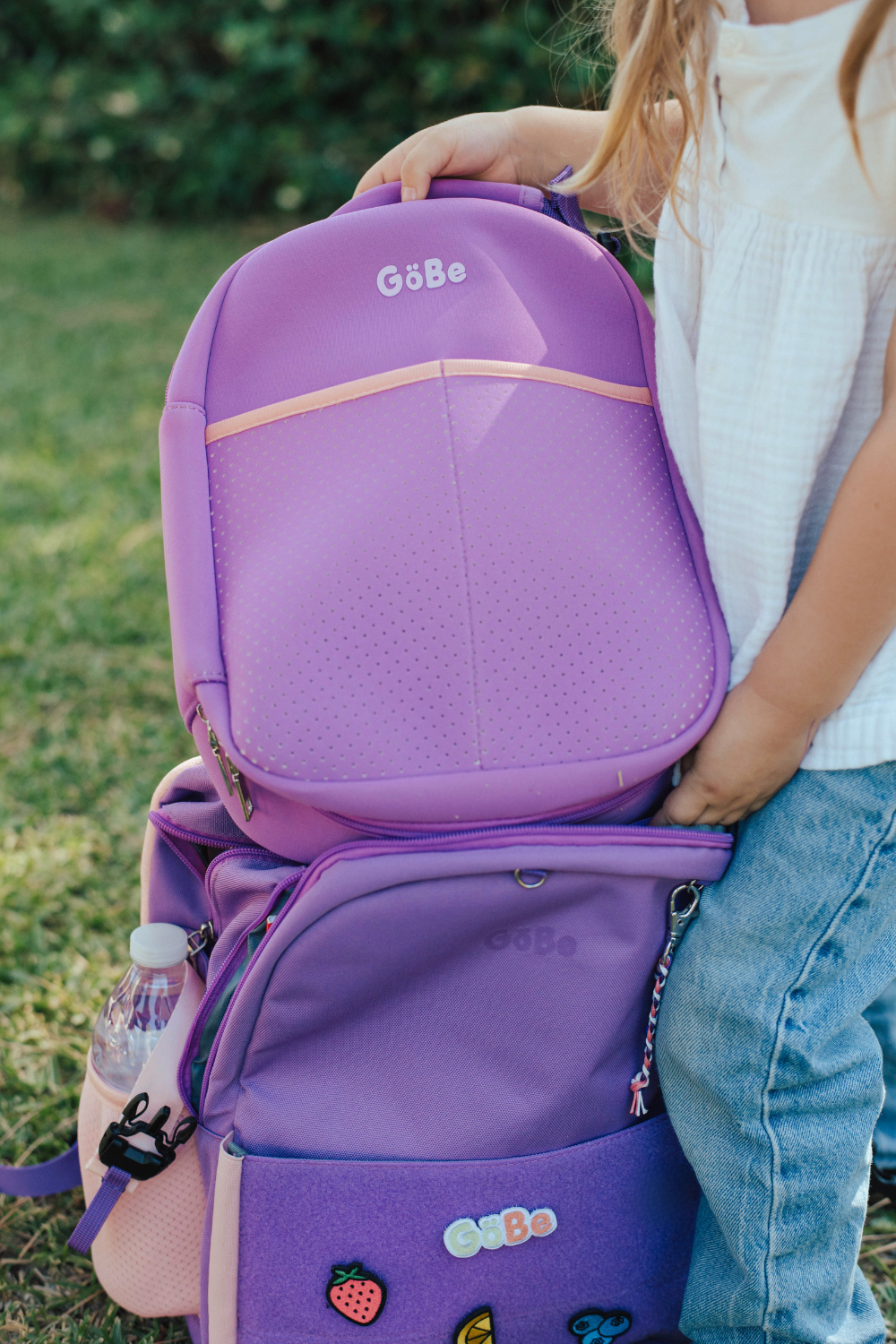 Purple GoBe lunch bag clipped to the front of a child's purple backpack